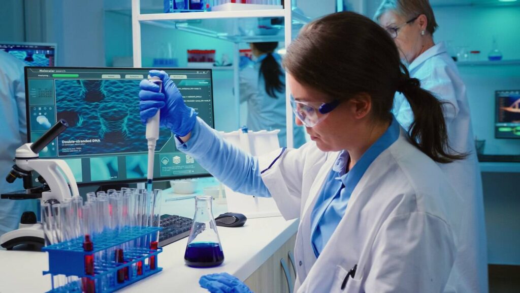 A female scientist conducts experiments using a pipette in a modern laboratory with computers displaying DNA structures.