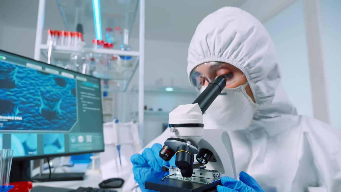 Scientist in full protective gear using a microscope in a high-tech laboratory.