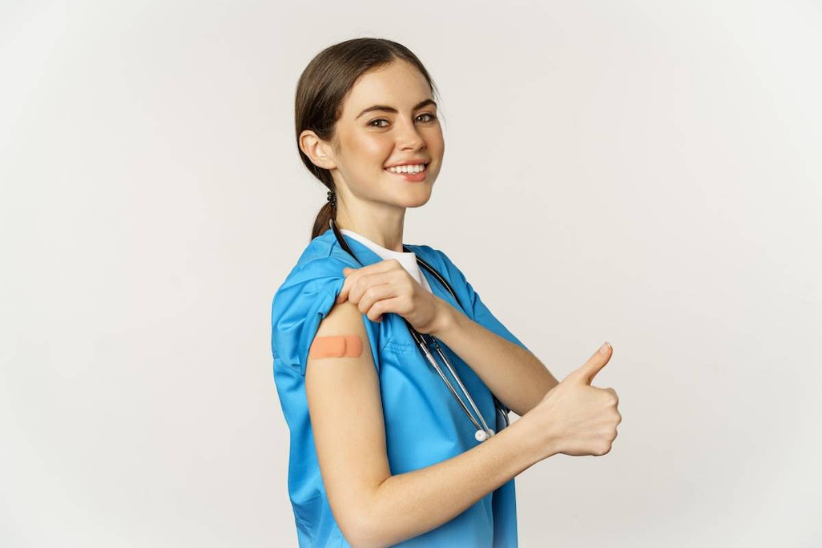 A healthcare worker in a blue scrubs shows a bandage on their arm
