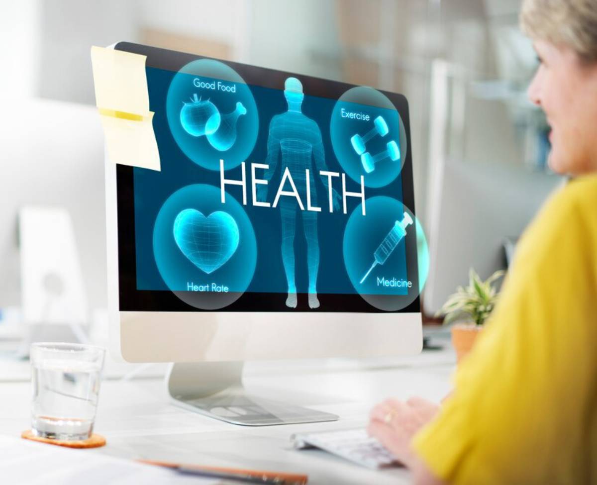 A senior woman looking at a computer screen displaying health-related graphics including a human silhouette and icons for exercise, good food, and medicine.