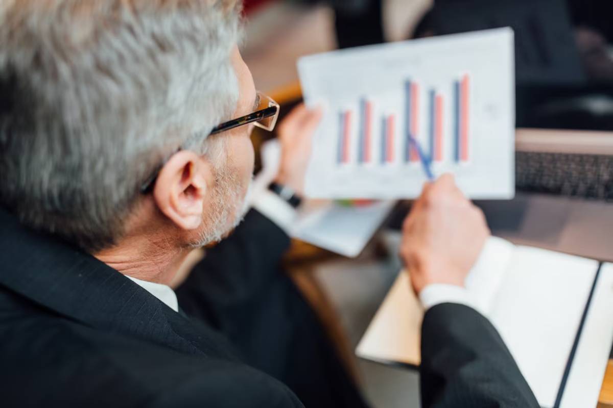 Senior man in glasses reading a financial report with bar graphs in an office setting.