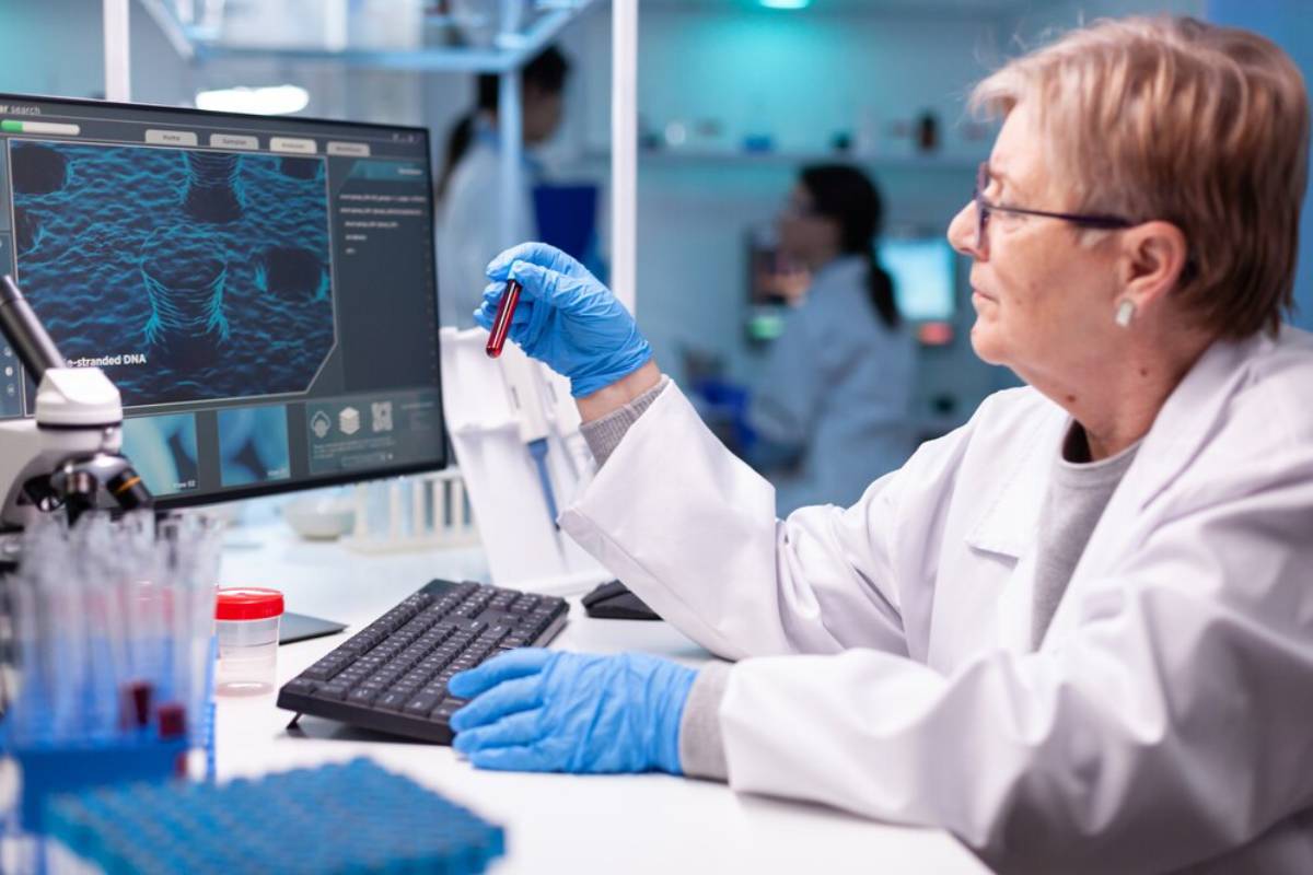Senior scientist examining a vial in a lab with a background screen showing DNA strands.