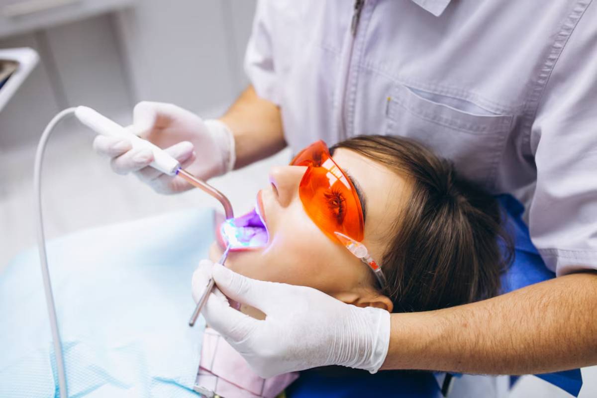 A dentist in gloves uses a dental tool on a patient lying back in a dental chair