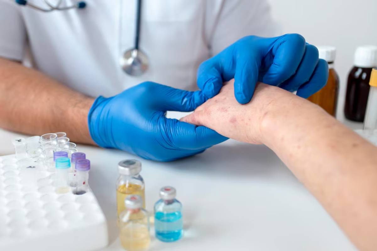 A healthcare professional in blue gloves performs a procedure on a patient's wrist, surrounded by test tubes and medication vials