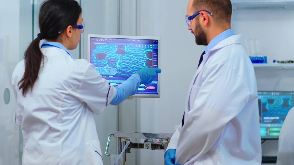 Two scientists analyzing a 3D molecular structure on a digital screen in a laboratory.