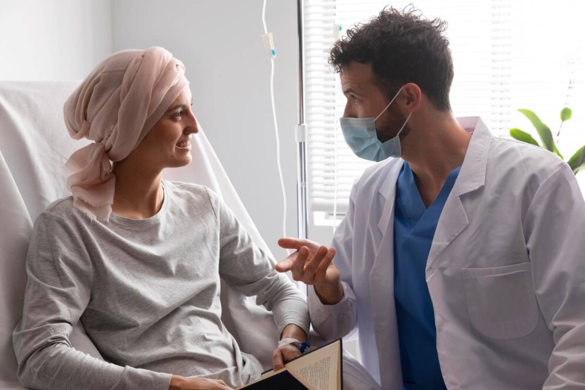 A female patient in a headscarf smiles at her male doctor during a consultation in a bright hospital room.