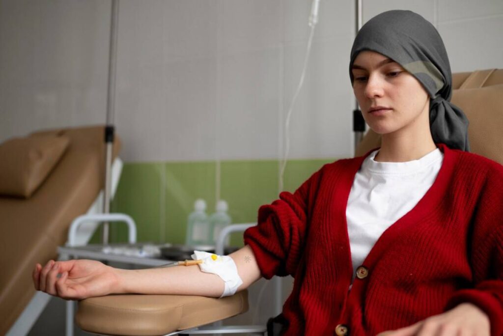 Young woman in a headscarf receiving chemotherapy, sitting in a hospital chair, looking thoughtful.
