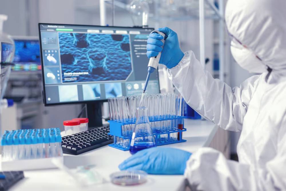 Scientist in protective gear pipetting samples in a laboratory with a digital screen displaying molecular structures.