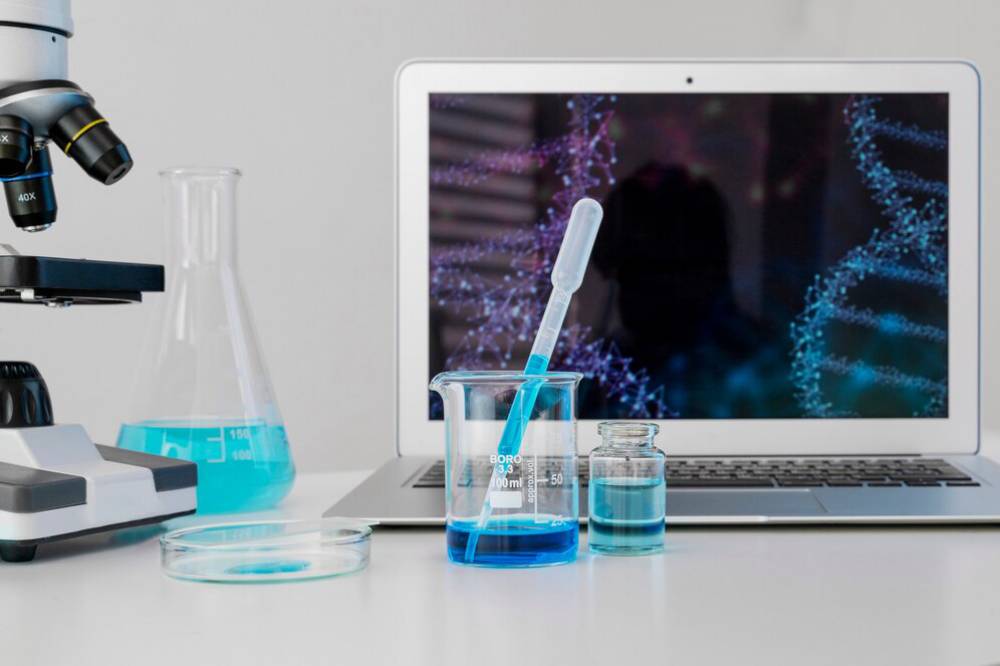 A laboratory setup with a microscope, blue chemical solutions, beakers, and a laptop displaying DNA strands.