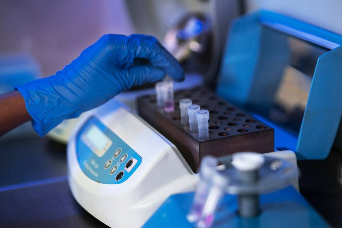 A scientist in blue gloves handling samples in small tubes at a laboratory workstation.