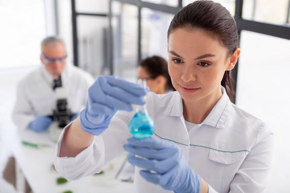 A female scientist examines a blue liquid in a flask in a laboratory setting.