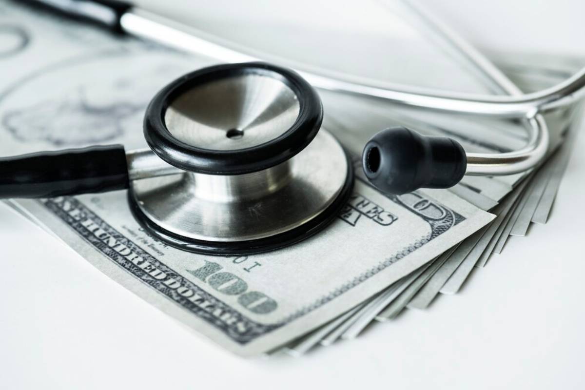 A stethoscope rests on a fanned stack of hundred-dollar bills, symbolizing the intersection of healthcare and finance.