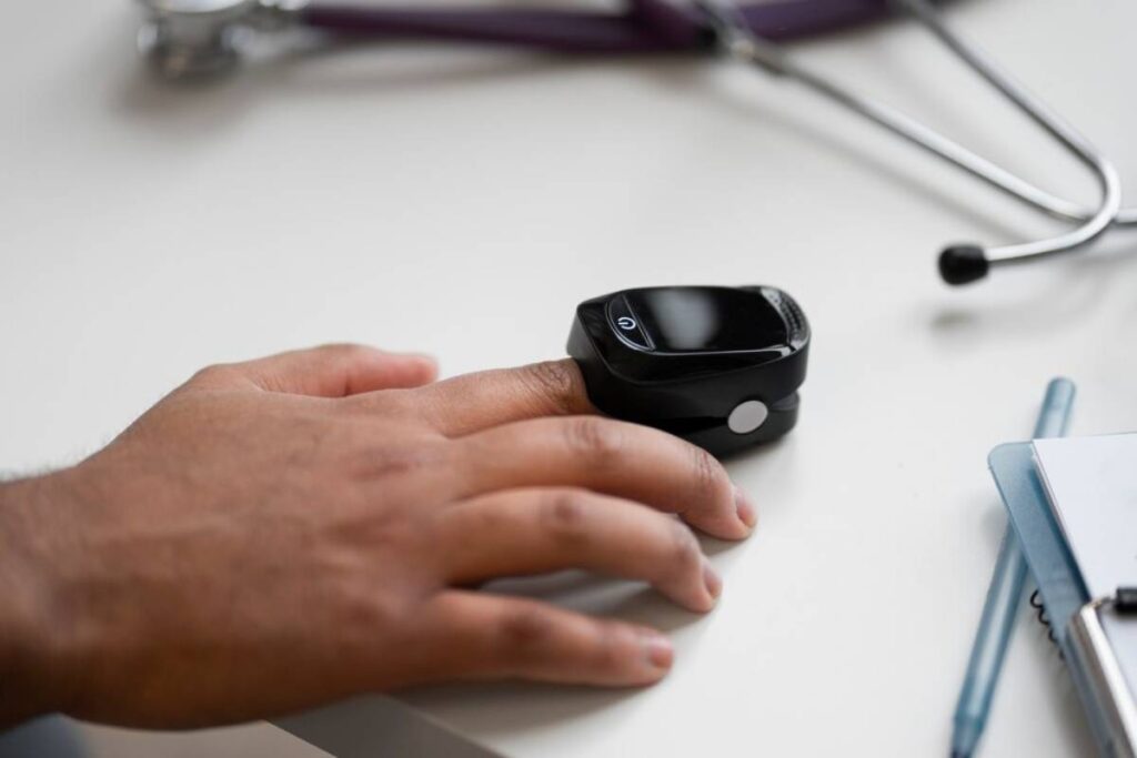 A person's hand next to a smartwatch on a desk with a stethoscope and notebook in the background.