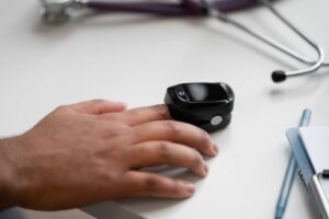 A person's hand next to a smartwatch on a desk with a stethoscope and notebook in the background.