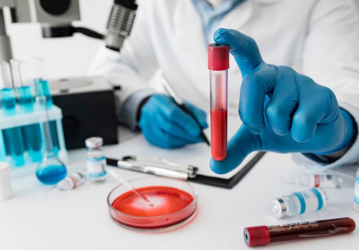 Scientist in a lab coat holding a test tube filled with red liquid, with laboratory equipment in the background.