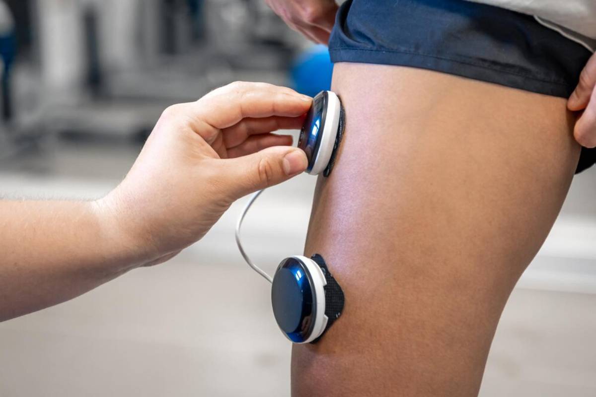 Physical therapist using a modern device on a patient's knee in a clinical setting.