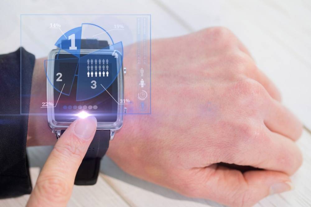 A person interacting with a futuristic smartwatch displaying holographic data charts.