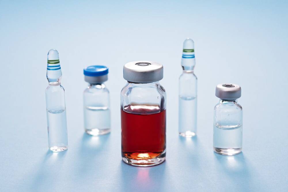 Several medical vials and bottles on a blue surface, one containing a red liquid.