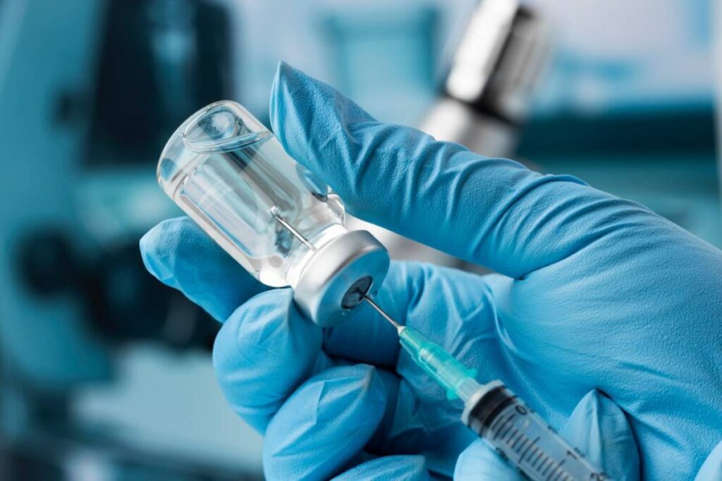 A healthcare worker fills a syringe with medicine from a vial, wearing blue gloves.