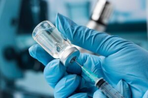 A healthcare worker fills a syringe with medicine from a vial, wearing blue gloves.