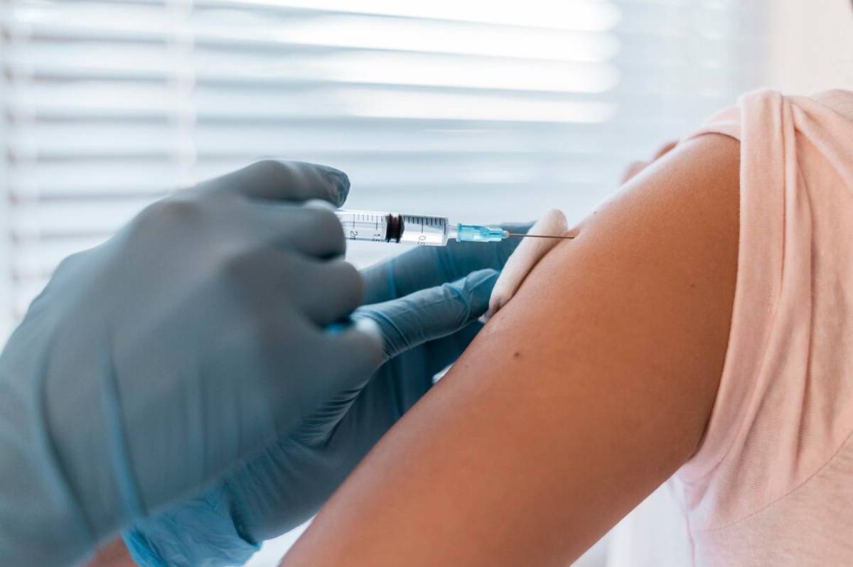 A healthcare professional in blue gloves administers an injection to a person's upper arm.