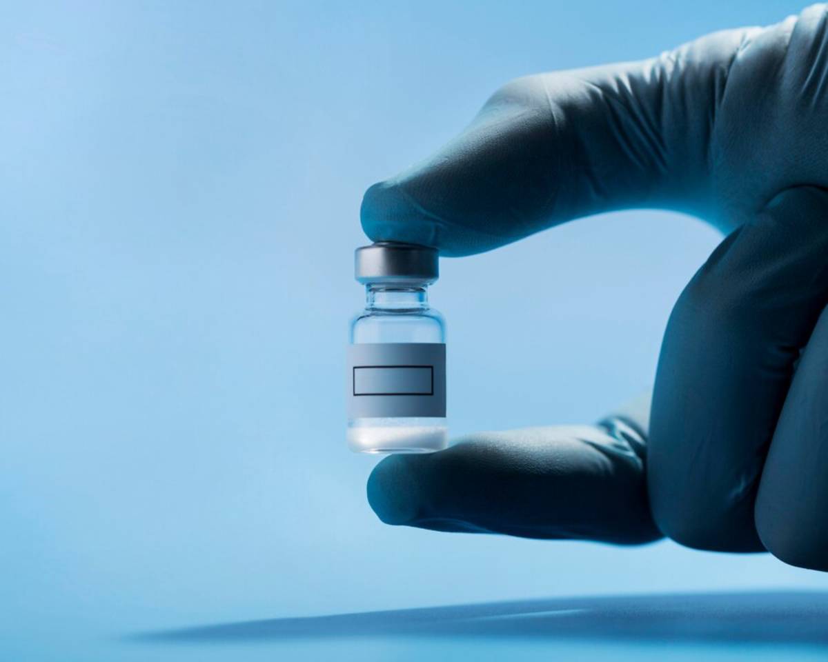 Gloved hand holding a small medical vial against a soft blue background.