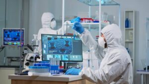 Two scientists in protective suits conducting experiments in a high-tech laboratory with computers displaying molecular structures.