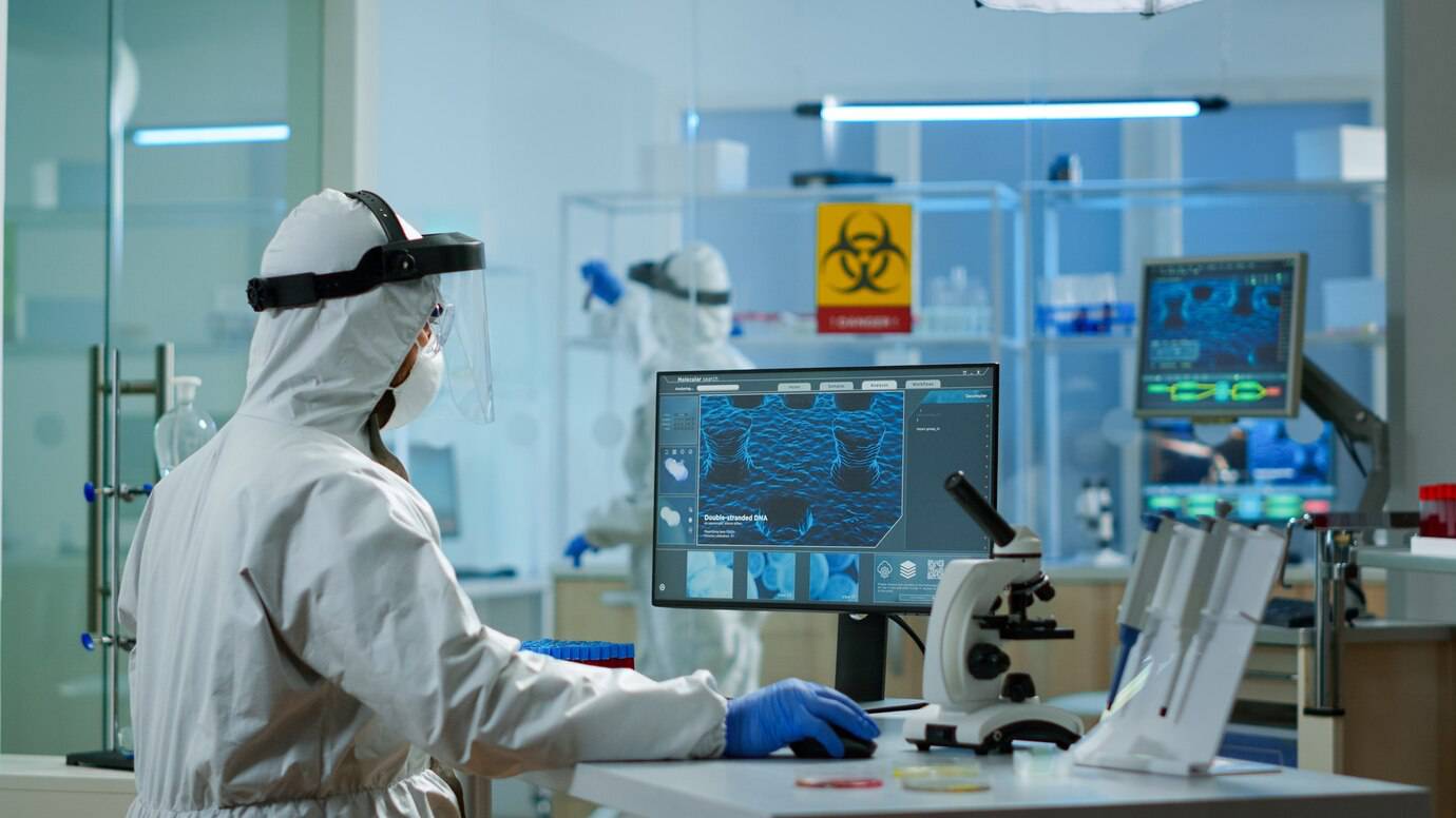 Scientist in protective gear analyzing DNA structures on a computer screen in a high-tech laboratory.